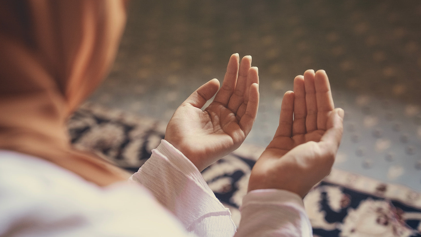 Frau mit Hijab beim Gebet – Sie macht Dua mit geöffneten Händen auf Gebetsteppich